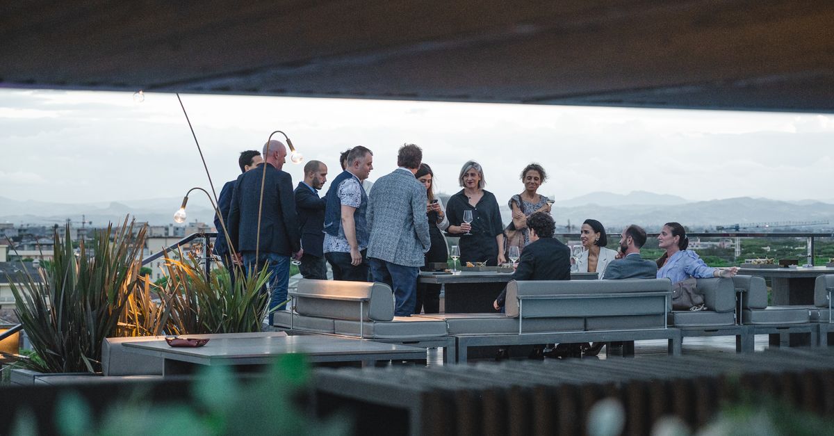 Erwachsene unterhalten sich in geselliger Runde auf einer Dachterrasse mit weitem Ausblick.